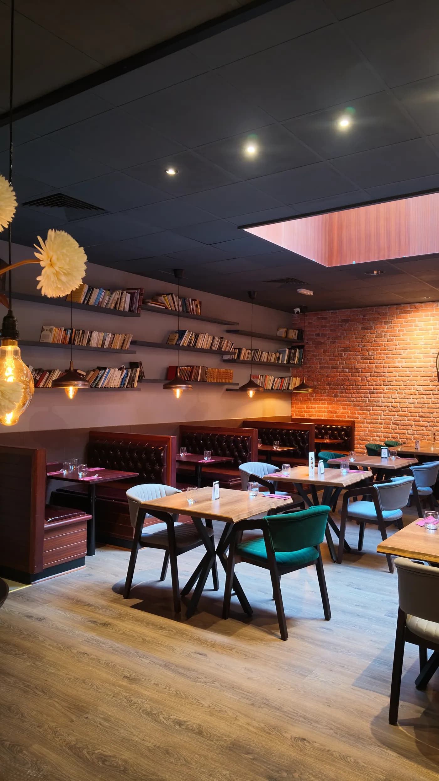 Salle du Manhattan Grill : banquettes en cuir capitonné, mur de briques, étagères de livres et lumière chaude des pendentifs.